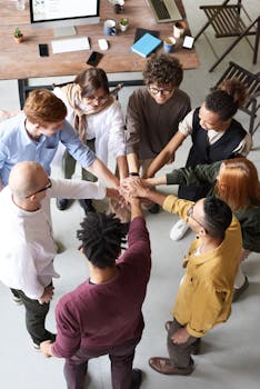 A diverse group of professionals joins hands in a team-building exercise indoors.